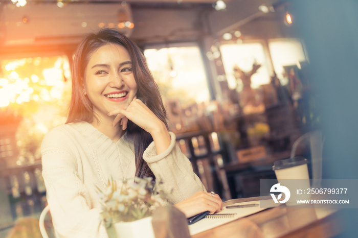 Happy young Asian woman working at a coffee shop with a sketchbook