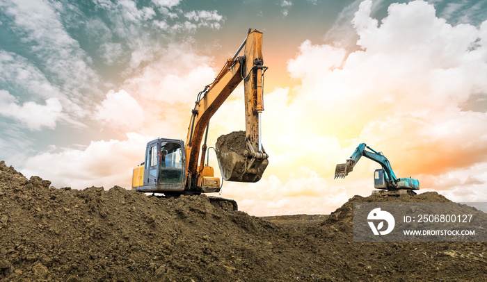 Two excavators work on construction site at sunset