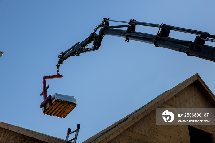 A wooden roof truss being lifted by a boom truck forklift in the roof a new home