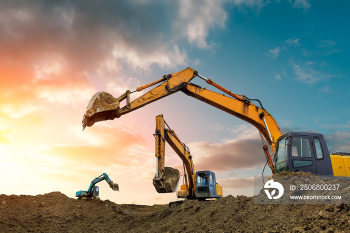 Three excavators work on construction site at sunset