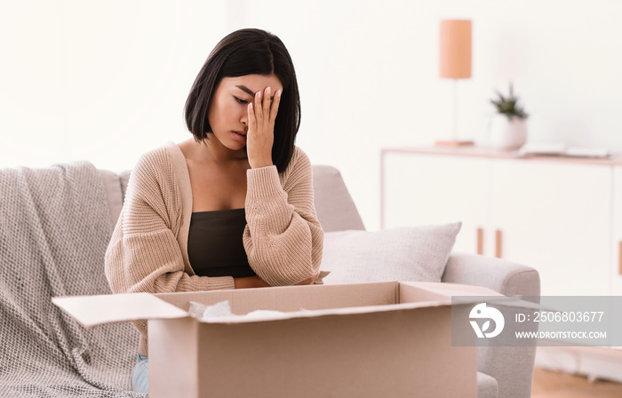 Sad young woman unpacking wrong parcel, delivery mistake