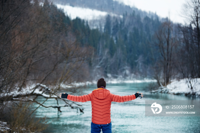 Man on solo camping trip. Winter gear walking along fast flowing rocky river, in scenic outdoor natu