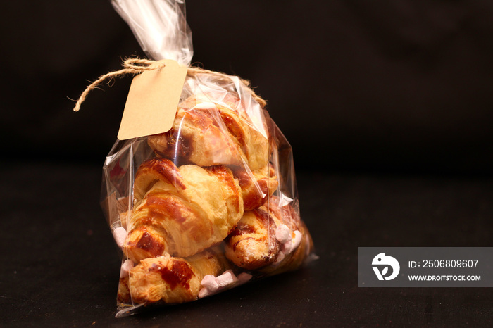 Fresh homemade French croissants with filling in a transparent cellophane bag with a tag on a black 