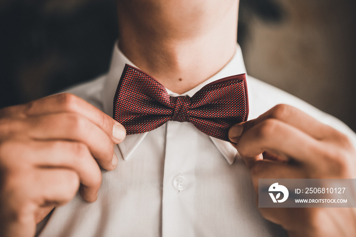 A man in a white shirt straightens his bow-tie