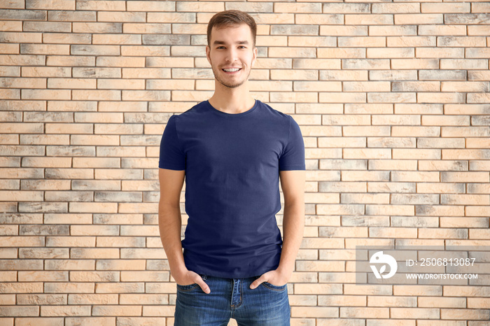 Young man in stylish t-shirt against brick wall. Mockup for design