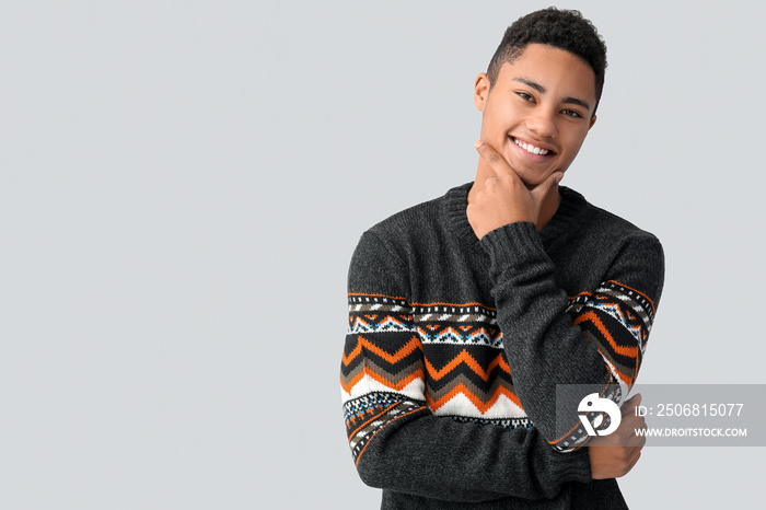 Handsome African-American guy in knitted sweater on light background