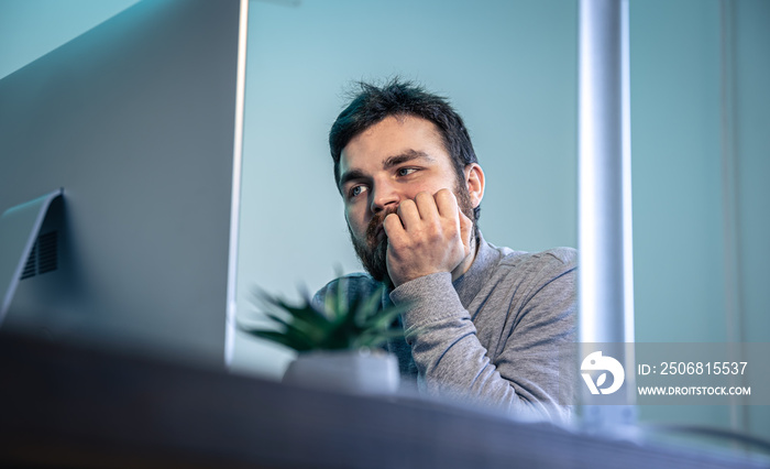 Tired bearded man looks at the computer screen.