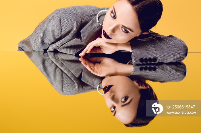 beautiful glamorous woman in formal wear looking at mirror reflection isolated on yellow