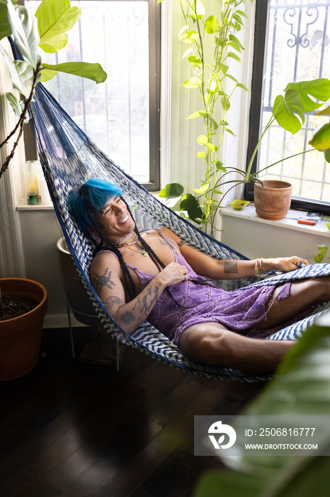 indigenous non-binary artist with blue hair relaxing in hammock