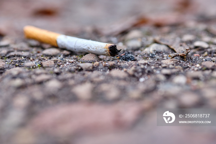 A thrown away used cigarette end with filter is lying on the ground on a footpath in winter. Seen in