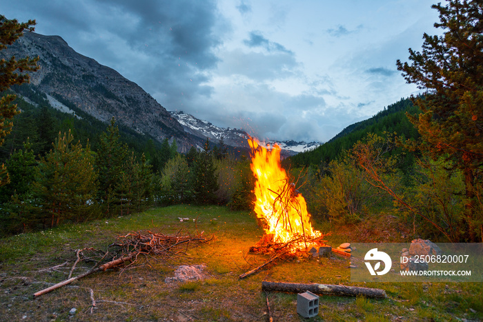 Burning camp fire into remote larch and pine tree woodland with high altitude landscape and dramatic