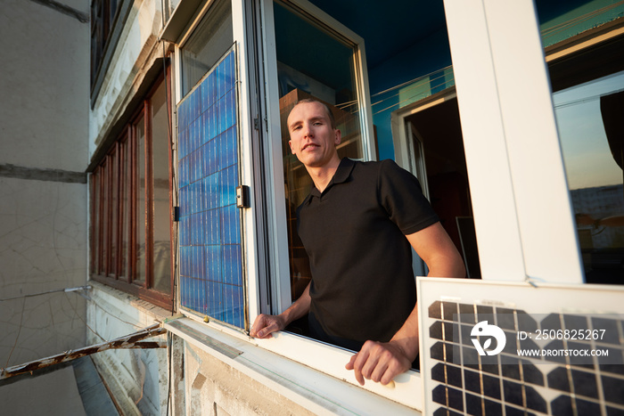 Smiling man on the balcony of a multi-storey building equipped with a solar panel, against a backgro