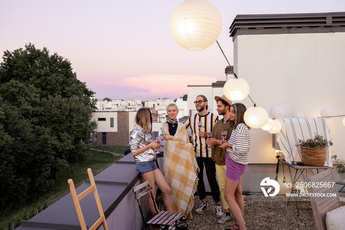 Young stylish friends hang out together talk and having fun on a rooftop party at dusk. Wide view wi