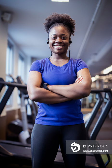 Low angle portrait of smiling female athlete with arms crossed standing in gym