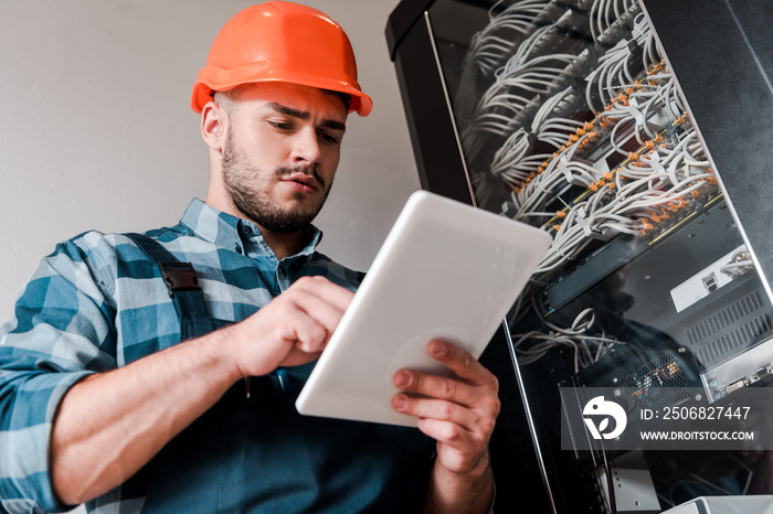 low angle view of handsome bearded technician using digital tablet