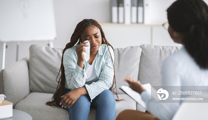 Unhappy black female client consulting psychologist, crying at medical office, banner design