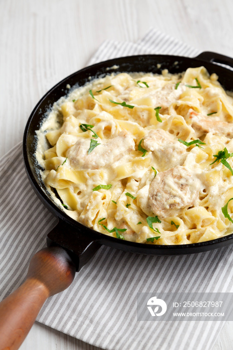 在铸铁平底锅中，白色木质背景，低角度视角，自制鸡肉Fettuccine Alfredo。