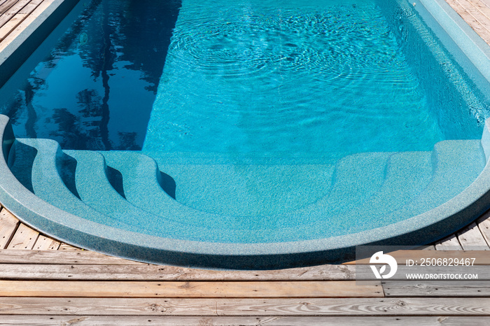 新的现代玻璃钢游泳池入口台阶，上面有干净、新鲜、清爽的蓝色水