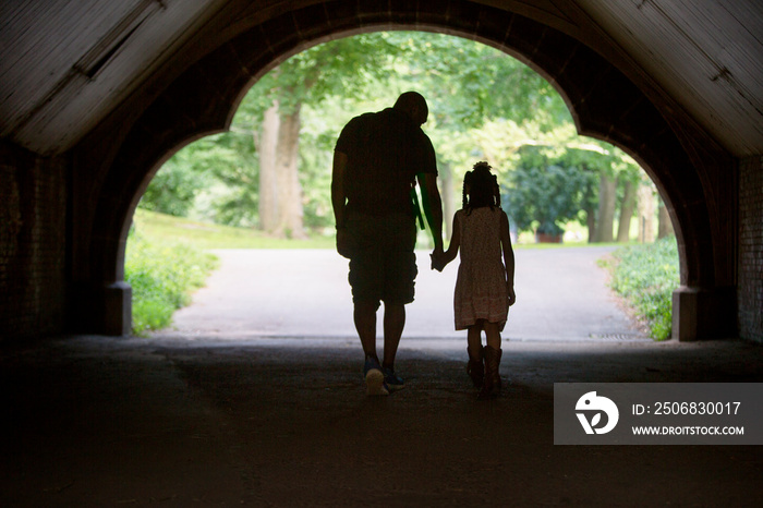 Silhouette of man walking in tunnel in park with daughter (6-7) holding hands