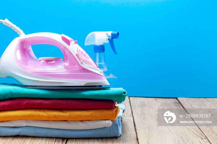 Pile of colorful clothes and irons,spray bottles,on wooden plank ,blue color background