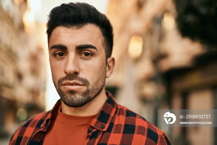 Young hispanic man with serious expression standing at the city.