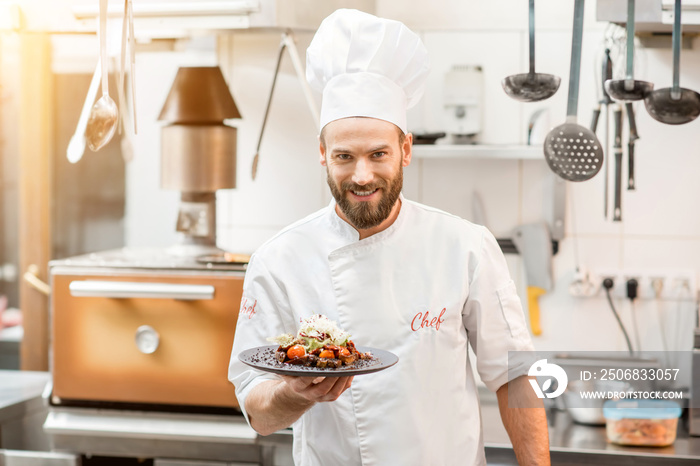 Portrait of chef cook in uniform standing with delicious dish at the kitchen