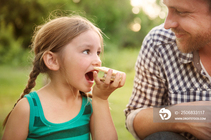 Smiling father and daughter having smore outdoors