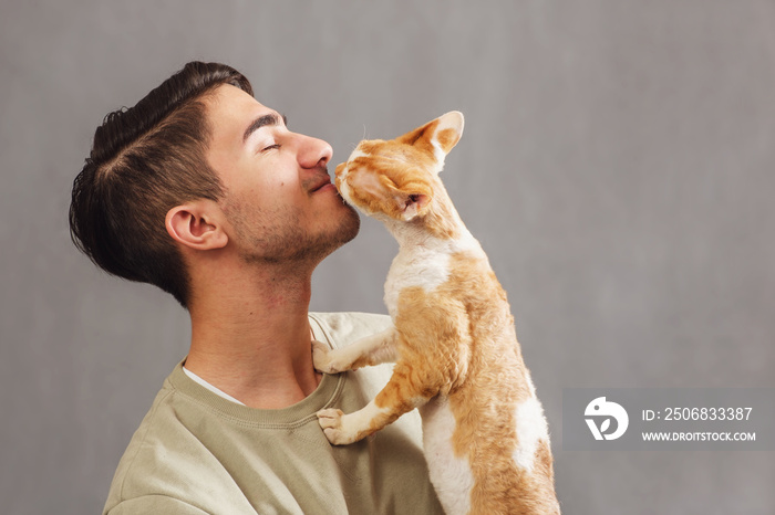 Side view of smiling young handsome man with closed eyes holding and kissing muzzle cute Devon rex c