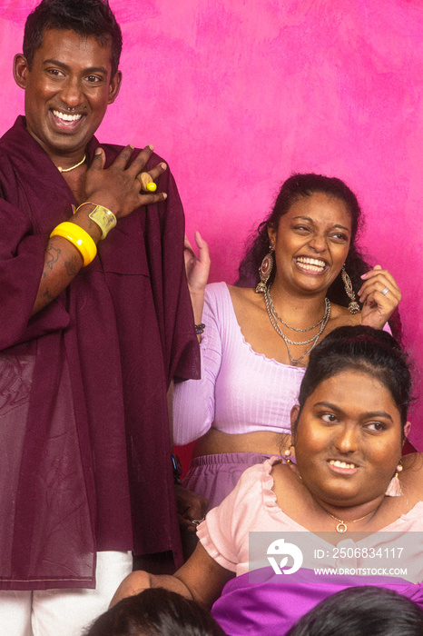 Group of Malaysian Indian individuals posing and laughing together against a red background, dressed