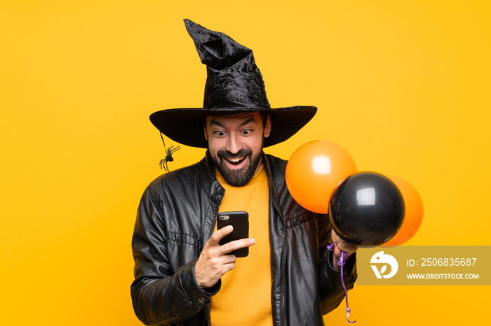 Man with witch hat holding black and orange air balloons for halloween party surprised and sending a