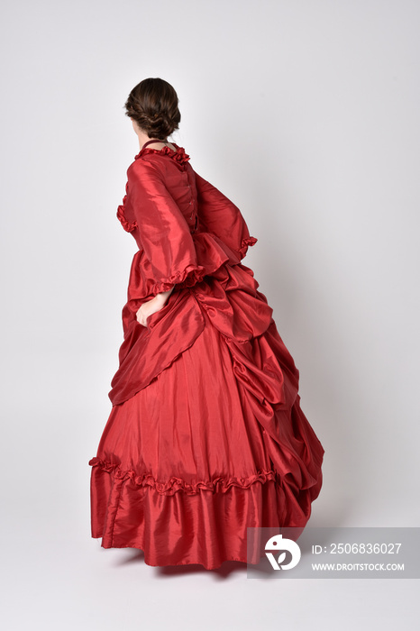 一位身穿红色丝绸维多利亚礼服的深色女孩的全长肖像。站立姿势，背部