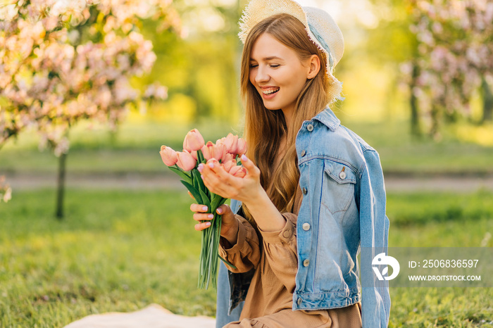 美丽的年轻女子戴着帽子，带着一束春花，在樱花园里