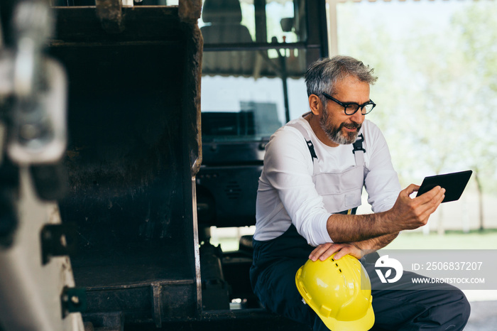 worker sitting on excavator using tablet