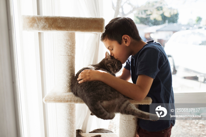 男孩站在家里亲吻躺在架子上的猫的侧视图