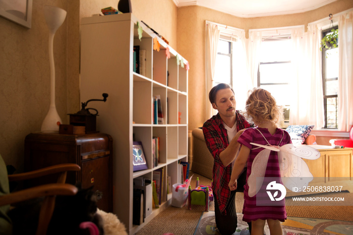 Father dressing her daughter in fairy costume at home