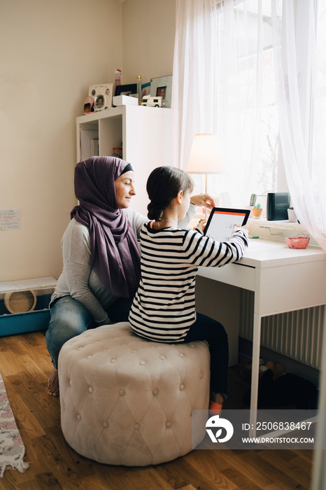 Mother assisting girl in doing homework through digital tablet at bedroom