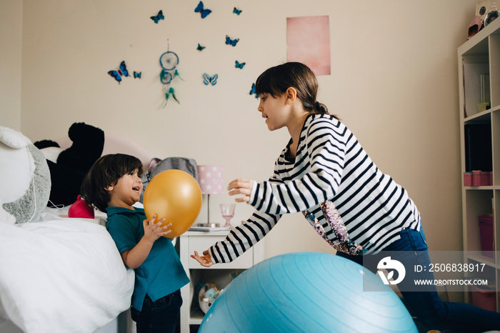 Siblings playing with balloon in bedroom at home