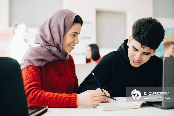 Smiling classmates reading book while studying together at desk in university