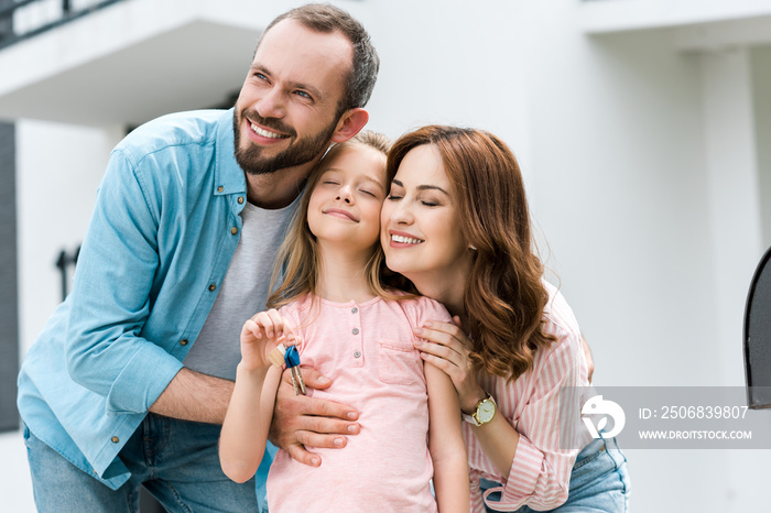 happy man standing with cheerful wife and kid with key