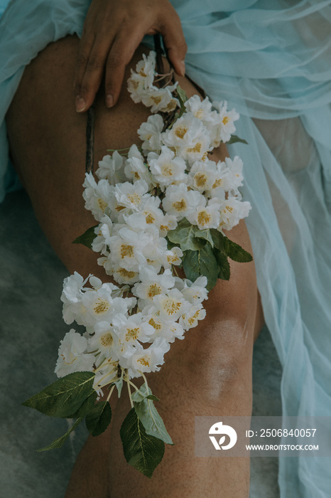 close up of East Indian woman holding white flowers on thigh surrounded by blue fabric