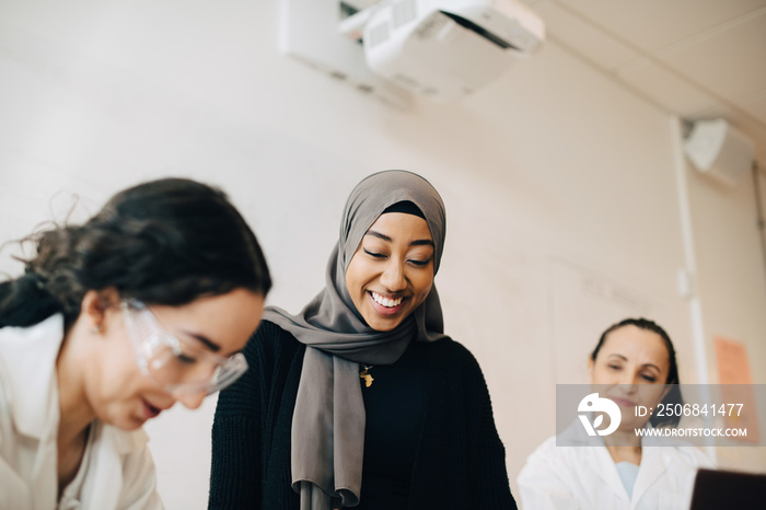 Teacher looking at smiling teenage girls experimenting during science class