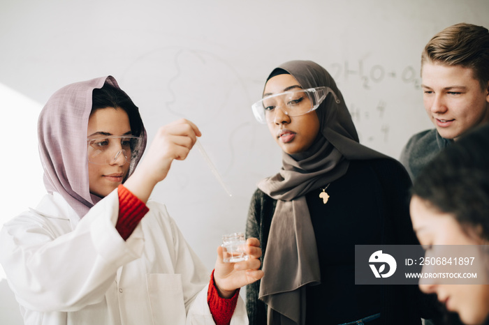 Classmates learning chemistry with teenage girl wearing hijab at university