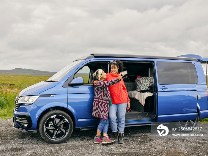 Female couple taking selfie in front of van