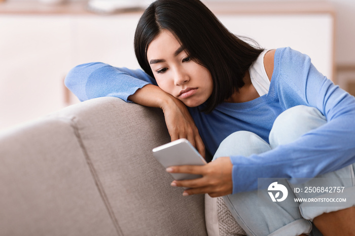 Frustrated lady checking mobile phone sitting on the couch