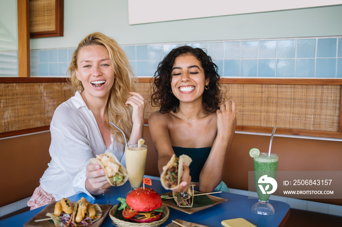 Cheerful multiethnic female friends laughing during lunch in summer cafe