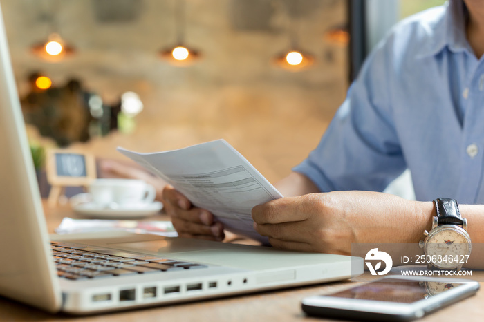 Businessman using laptop while looking at invoice.