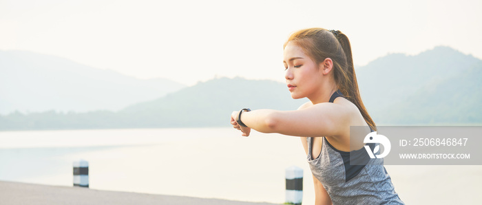 Young asian woman looking the sports watch and checking her performance. on the road.