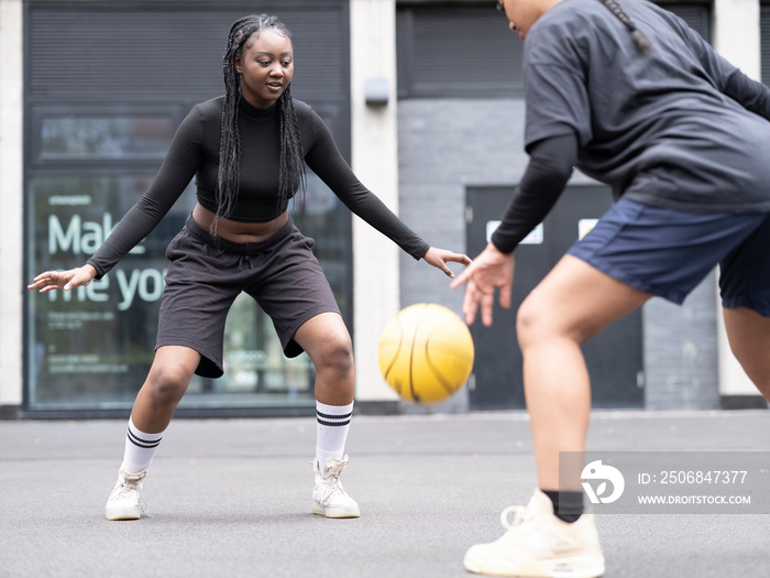 Two female friends playing basketball outdoors