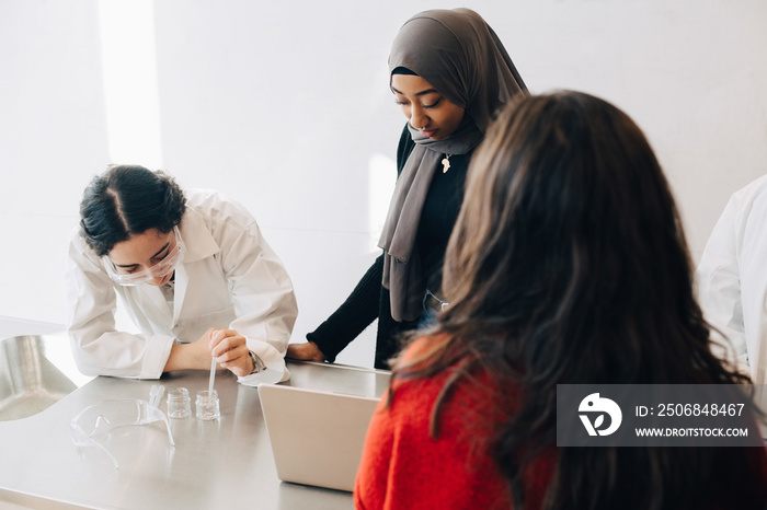 Classmates looking at teenage girl doing scientific experiment in laboratory