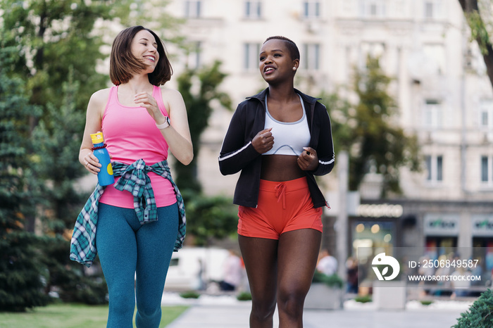 穿着运动服在城市里跑步的快乐微笑的朋友们在讨论。多民族女性正在健身
